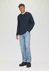 Granatowa koszula z długim rękawem z guzikiem, zestawiona z jasnoniebieskimi przetartymi dżinsami i czarnymi sznurowanymi butami. Prosty, teksturowany design.