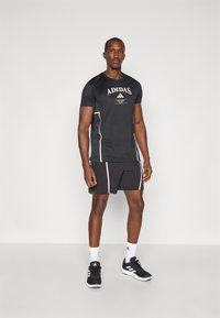 Fekete sportpóló és rövidnadrág fehér kiemelésekkel. Az ingem Adidas logóval rendelkezik. Fekete sportcipővel és fehér zoknival viselve.