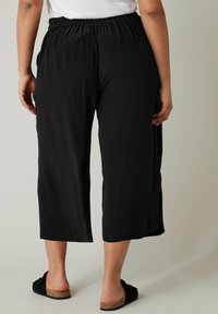 Zwarte cropped broeken met een elastische tailleband, een gladde textuur en zijzakken, gecombineerd met platte, open schoenen.
