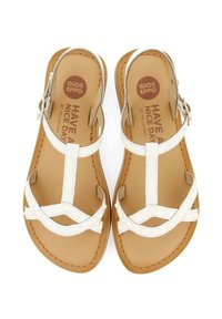 Sandalias de cuero blanco con un diseño de tiras en T, punta redonda y acentos circulares en las correas. Plantilla texturizada con una suela marrón.