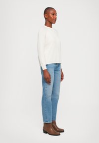 Krem lett genser, avslappet passform, kombinert med lyseblå rette jeans og brune ankelstøvler. Enkel, teksturert finish.