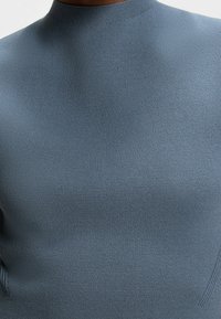 Svetle modrý svetr s vysokým límcem z texturovaného pleteného materiálu. Přiléhavý střih s žebrovanými detaily po stranách. Celkově hladký povrch.