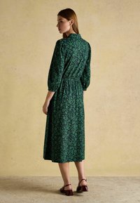 Roheline lillemustriga midi kleit puffvarrukatega ja elastse vööga. Kandmiseks burgundi värvi plokk-kanna sandaalide juurde. Tekstuuriga beež taust.