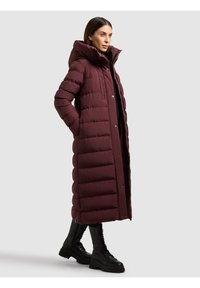 Bordó pufi kabát magas gallérral, gombos rögzítéssel és látható varrással. Fekete ruházat felett viselve, fekete fűzős csizmával kombinálva.