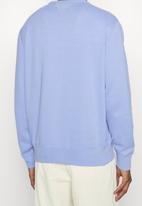 Fleece-tröja i ljusblått, med långa ärmar, rundad halsringning och ribbmuddar. Slät textur med minimal sömdetaljering.