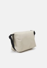 Borsa sintetica beige con una texture morbida, forma rettangolare, tracolla nera e chiusura con zip. Presenta un delicato dettaglio di cucitura sul lato.