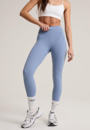 Light blue leggings made of stretchy material, featuring a high waistband and smooth finish. Paired with white socks and athletic shoes.