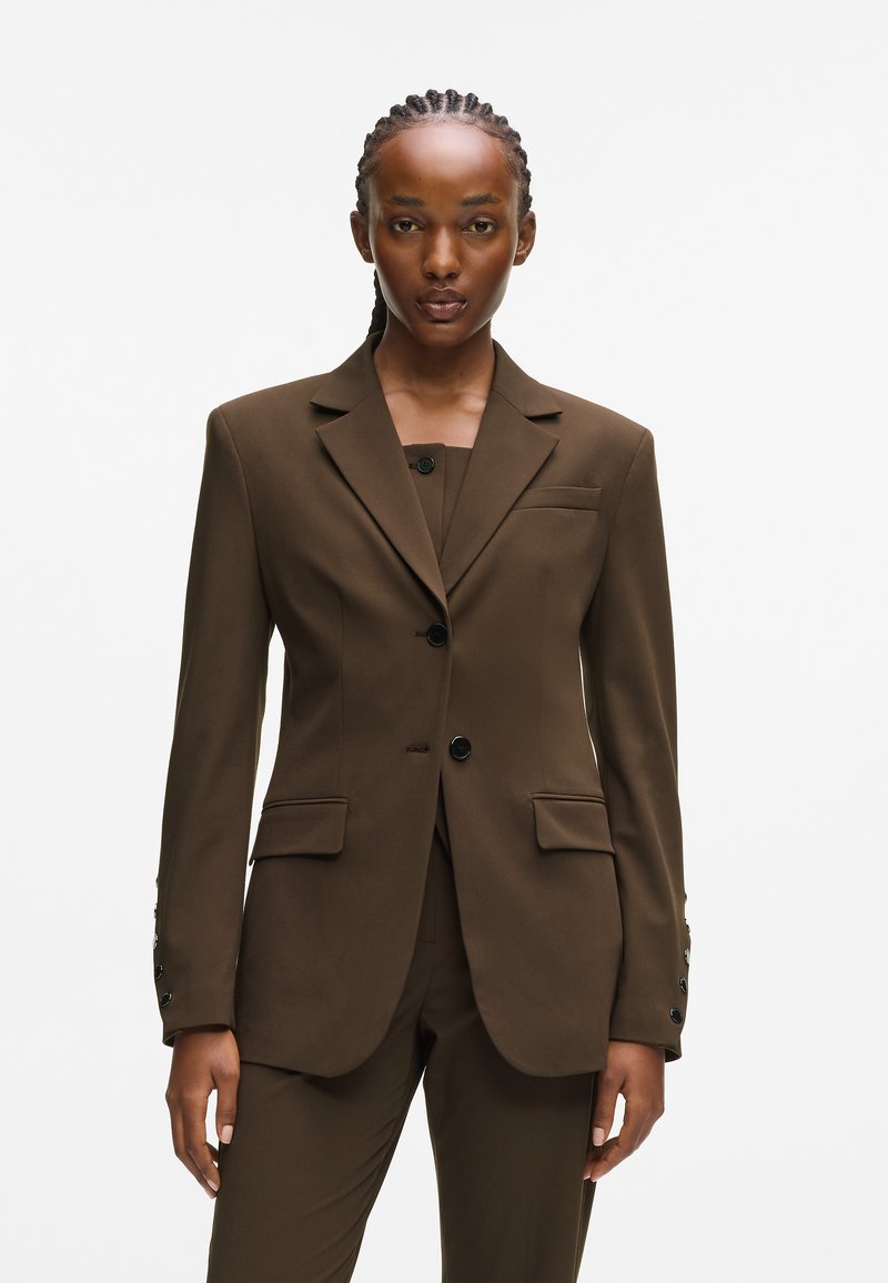 Brauner taillierter Blazer aus glattem Stoff. Verfügt über einen Reverskragen, eine einreihige Knopfleiste mit zwei Knöpfen und Fronttaschen.