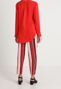 Röd blus med långa ärmar och rundad fåll. Matchad med rosa och svarta vertikalt randiga vida byxor. Svarta sandaler med kraftig klack.