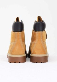 Stivaletti alla caviglia in suede color sabbia con colletto in pelle nera, caratterizzati da cuciture bianche a contrasto e suole in gomma marrone. Design con rinforzo sul retro.