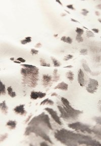 Tessuto di cotone con uno sfondo crema, caratterizzato da un motivo di macchie e vortici astratti in nero e grigio, con una texture liscia e una caduta morbida.