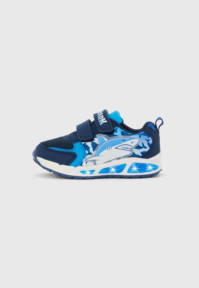 Scarpa da ginnastica blu per bambini con grafica di squalo sul lato, due cinturini a velcro e dettagli della suola illuminati su sfondo semplice.