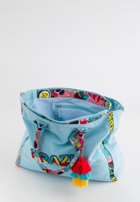 Bolsa de mano de algodón azul con correas estampadas coloridas y borlas. Cuenta con un bolsillo interior con cremallera y la palabra "BRAZIL" bordada en el frente.