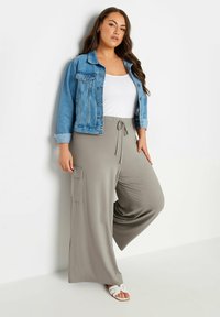 Ljusblå denimjacka över en vit linne, kombinerad med grå vida byxor med dragsko i midjan och sidofickor. Vita sandaler.