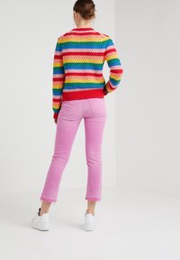 Suéter de rayas multicolores con diseño de tejido texturizado, combinado con jeans cortos rosas y zapatillas blancas.