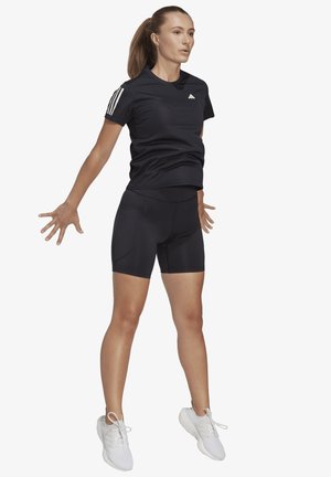 Čierne športové tričko s kratkým rukávom a tromi bielymi pruhmi na ramenách v kombinácii s čiernymi priliehavými šortkami. Biely tenisky.