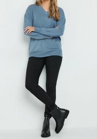 Ljusblå V-ringad tröja med långa ärmar, kombinerad med svarta leggings och ankelstövlar. Tröjan har ribbade fårribbsdetaljer.