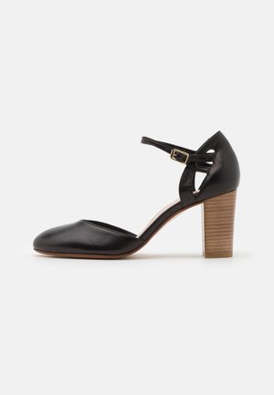 Chaussure à talon haut en cuir noir avec un bout en amande, bride de cheville ajustable et un talon en bois texturé.