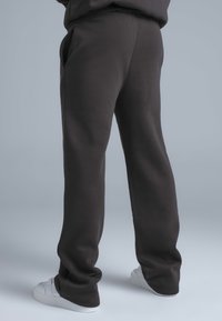 Donkergrijze joggingbroek van een zachte, gestructureerde stof met een losse pasvorm en zijzakken, gecombineerd met witte sportschoenen.