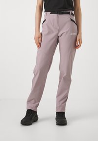 Light pink outdoor pants with a smooth texture, featuring black accents, side pockets, and a belt. Worn with black hiking shoes.