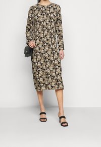 Blommig midikjol med långa ärmar, svart bakgrund, krämfärgade och gyllene blommor, rund halsringning och avslappnad passform. Tillsammans med svarta klacksandaler.