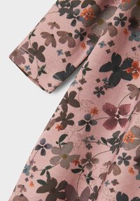 Kukallinen kangas vaaleanpunaisena, vihreillä, ruskeilla ja oransseilla yksityiskohdilla. Sisältää erilaisia kukkamalleja ja sileän, pehmeän tekstuurin.