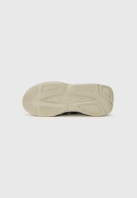 Såle av en sneaker med et teksturert beige gummimateriale med spor og mønstre for grep, preget logo i midten.