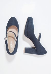 Chaussures à talons hauts en daim bleu marine avec un bout rond, une bride de cheville et un talon carré épais. Texture lisse avec des détails minimalistes.