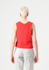 Red sleeveless top with a rounded neckline, made of soft fabric. The back features a simple design, paired with vertically striped pants.