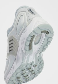 Light gray athletic shoe with mesh and synthetic materials. White rubber sole with textured grip and visible cushioning units.
