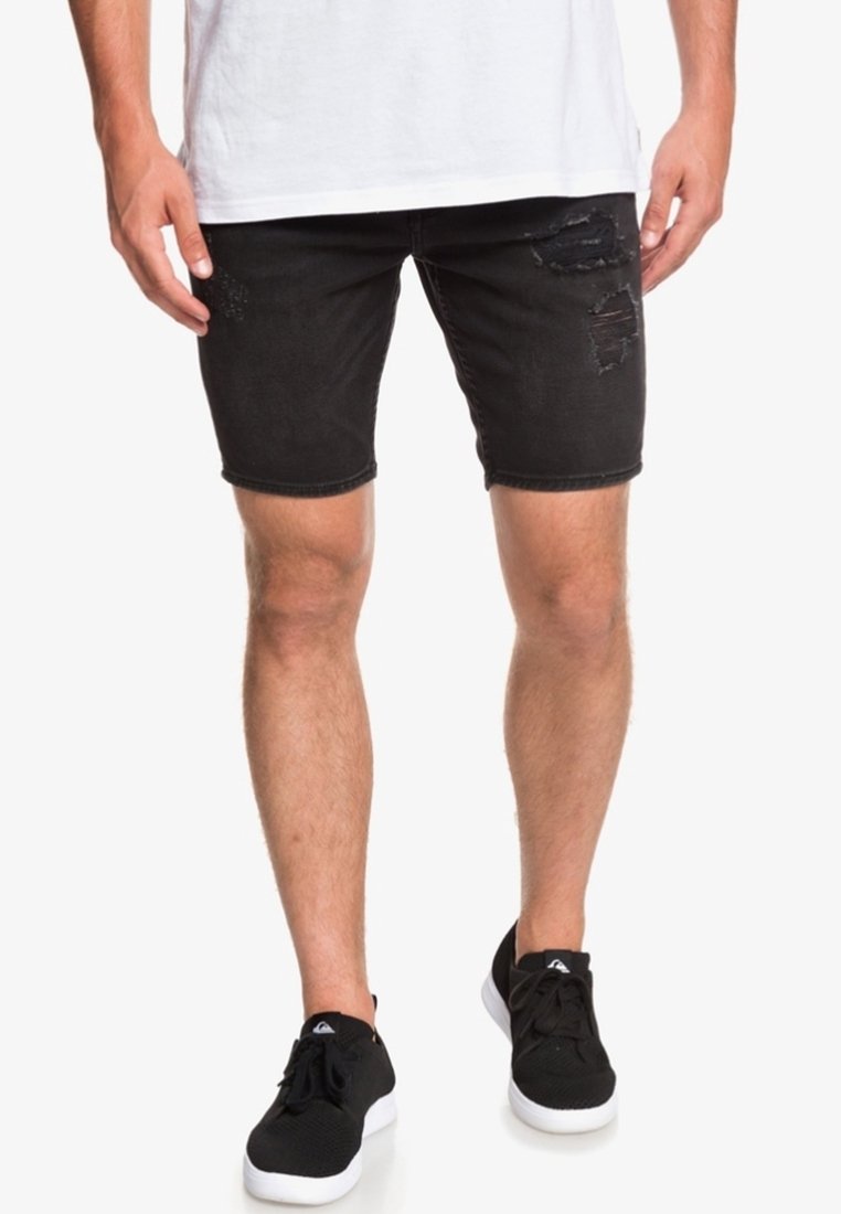 Mustat farkkushortsit, joissa on kulutettu yksityiskohtia, slim fit -mallilla ja suora helma. Yhdistetty valkoiseen t-paitaan ja mustiin lenkkikengiin.