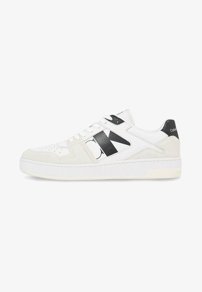 Zapatilla blanca hecha de cuero y ante, con un gran logo negro, cordones planos y una suela de goma texturizada.