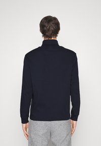 Námořnické polokošile s dlouhým rukávem a límcem, vyrobené z hladkého materiálu; má rovný lem a přiléhavé rukávy.