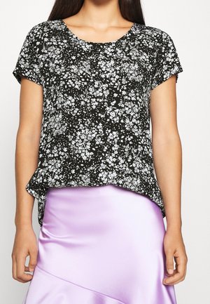 Femme portant un haut noir à manches courtes avec un motif floral blanc et une jupe en satin lavande brillante, montrée du cou aux hanches.