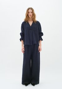 Completo di lino navy con una maglia ampia a V e maniche svasate, abbinato a pantaloni a gamba larga. Texture morbida e design rilassato.