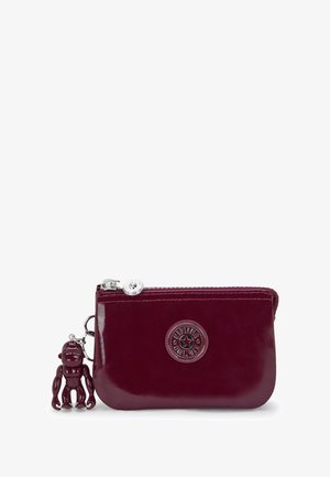 Portafoglio in pelle bordeaux con chiusura a zip, logo impresso e ciondolo decorativo a forma di scimmia. Texture liscia e forma rettangolare compatta.
