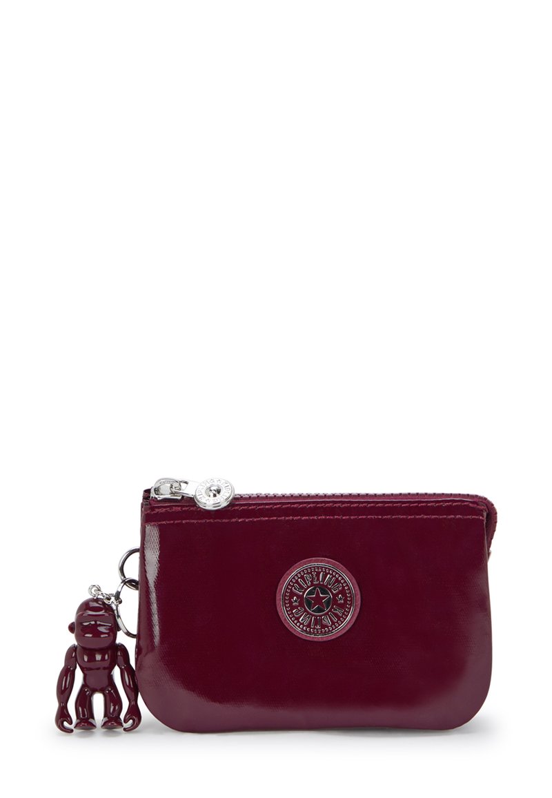 Portafoglio in pelle bordeaux con chiusura a zip, logo impresso e ciondolo decorativo a forma di scimmia. Texture liscia e forma rettangolare compatta.