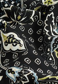 Tissu noir avec un motif floral en blanc, crème et vert, accompagné de formes géométriques, mettant en valeur un tissage texturé et des couleurs vives.