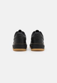 Baskets Nike noires avec une tige en cuir texturé, un col rembourré, des détails cousus et une semelle en caoutchouc gomme. Vue de dos.