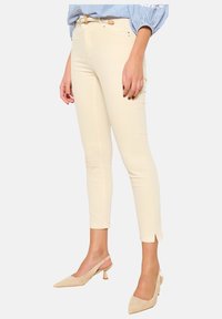 Pantalones ajustados color crema con una textura suave, aberturas en los tobillos y una cintura de altura media. Combinados con tacones beige de punta afilada.