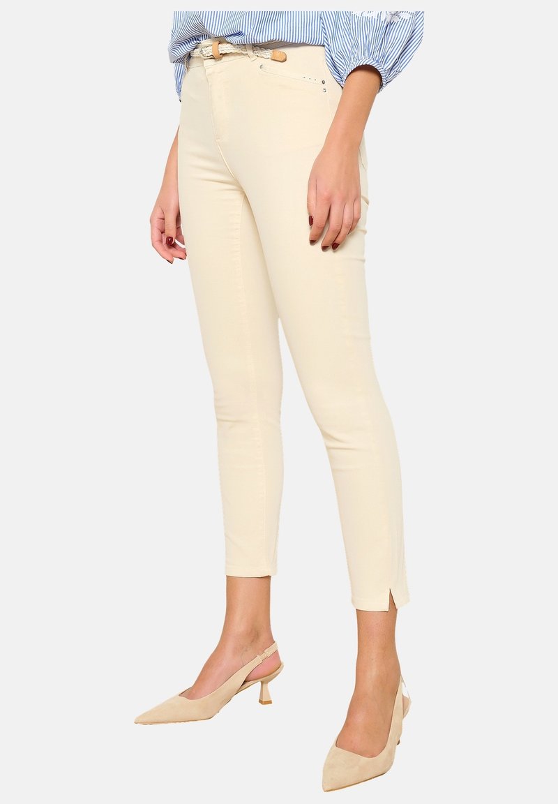 Pantalones ajustados color crema con una textura suave, aberturas en los tobillos y una cintura de altura media. Combinados con tacones beige de punta afilada.