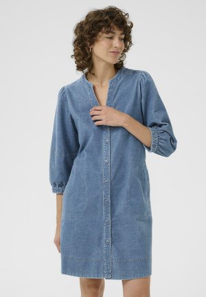 Robe en denim bleu clair avec des manches bouffantes trois quarts, devant à boutons, deux poches latérales et coupe droite. Texture douce et design simple.