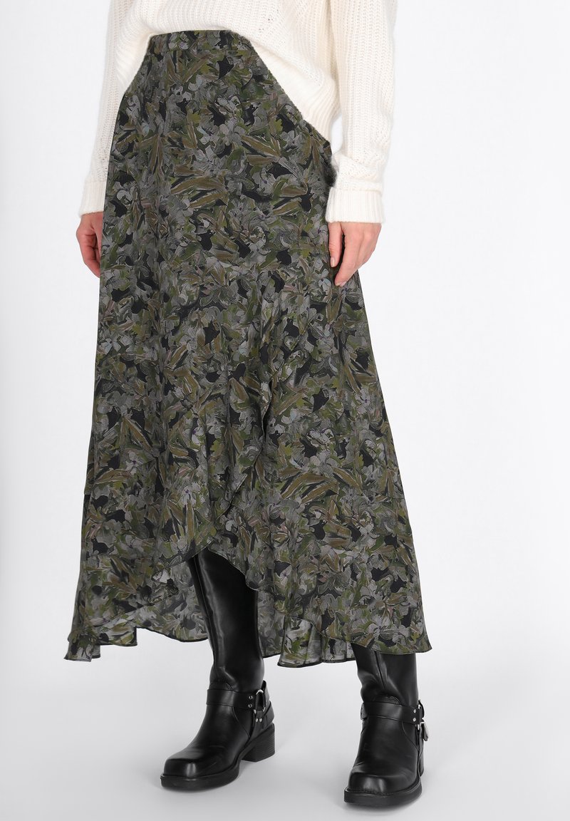 Persona che indossa una gonna asimmetrica verde a fiori, un maglione bianco a maglia e stivali in pelle neri al polpaccio con fibbie su uno sfondo bianco.