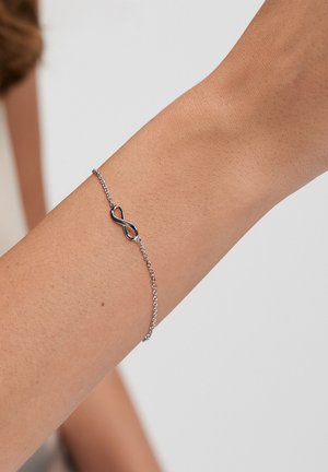 Silver chain bracelet featuring a black infinity symbol, highlighting a sleek design and smooth texture on the wrist.