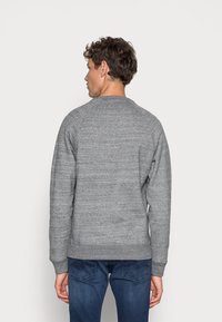 Grijze sweatshirt in een gestructureerde brei met een ronde hals, raglanmouwen en geribbelde manchetten en zoom. Draagt men met blauwe jeans.