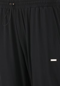 Schwarze Sporthosen aus strukturiertem Stoff, mit einem elastischen Taillenbund, Kordelzug und einem kleinen metallischen Logo-Detail.