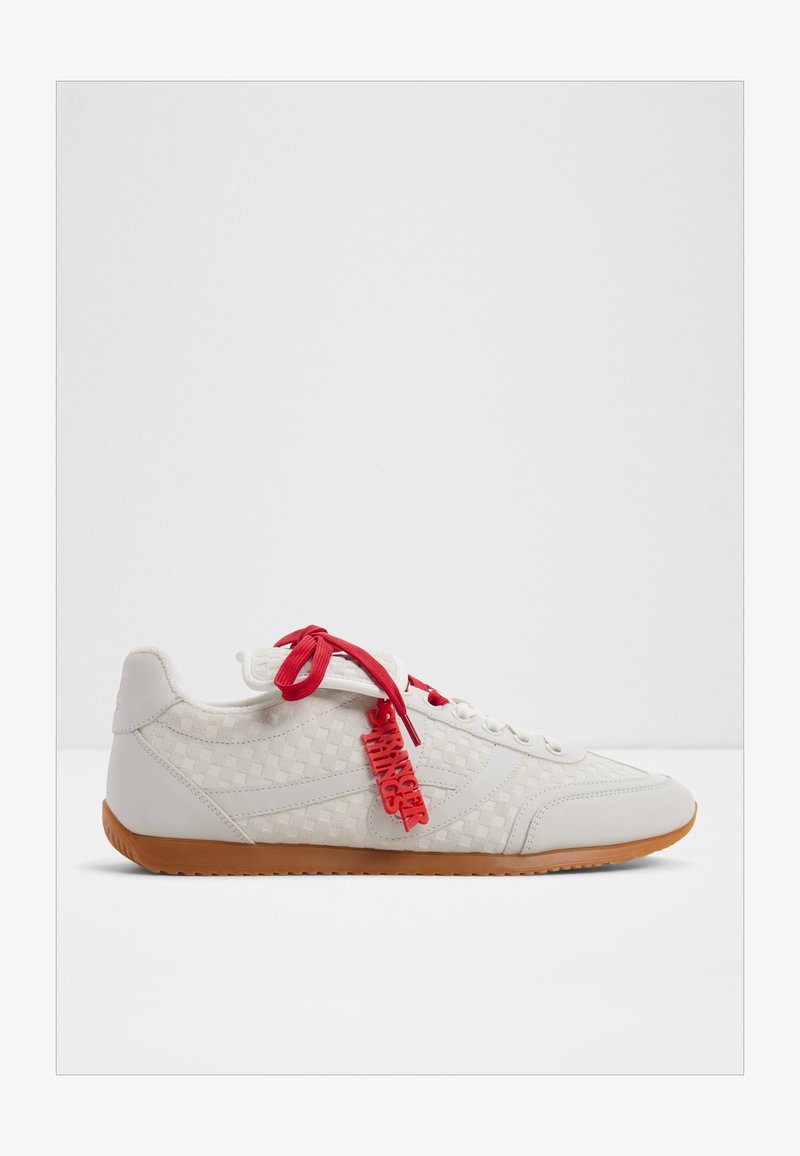 White low-top sneaker with a checkered pattern, gum sole, red laces, and a red tag hanging that reads "STRANGER THINGS."