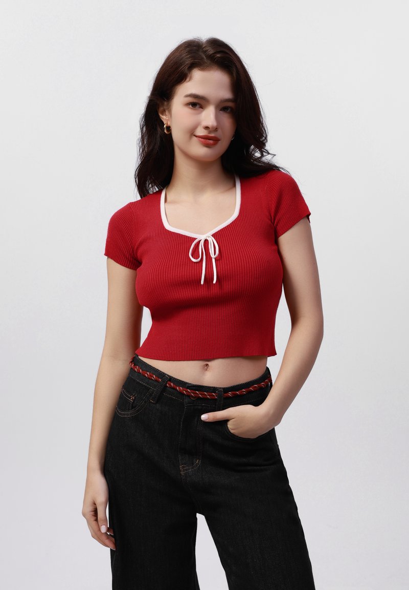 Top corto de canalé rojo con mangas cortas y escote cuadrado, que presenta un detalle de cordón blanco. Combinado con pantalones negros de talle alto.