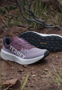 Zapatillas deportivas moradas con parte superior de malla, que presentan un destacado logo "TERREX", una suela blanca acolchada y una suela exterior negra texturizada.