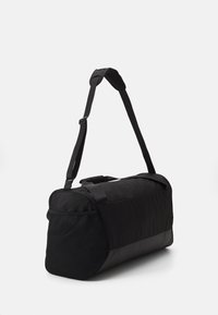 Bolsa de deporte negra con forma curva, fabricada en nylon, con un bolsillo lateral de malla, correa ajustable y asas dobles en la parte superior para un fácil transporte.